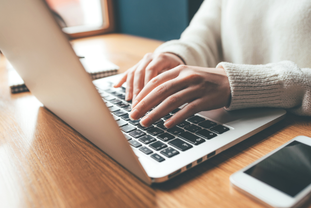 Person typing on a laptop keyboard with a smartphone nearby, representing digital commerce and online business solutions.