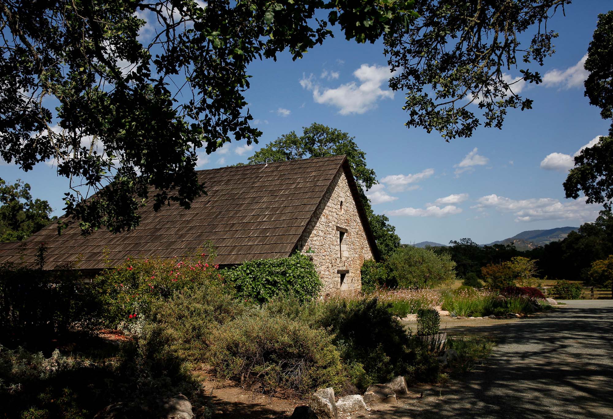 Scenic view of a stone cottage surrounded by lush greenery and trees under a blue sky.